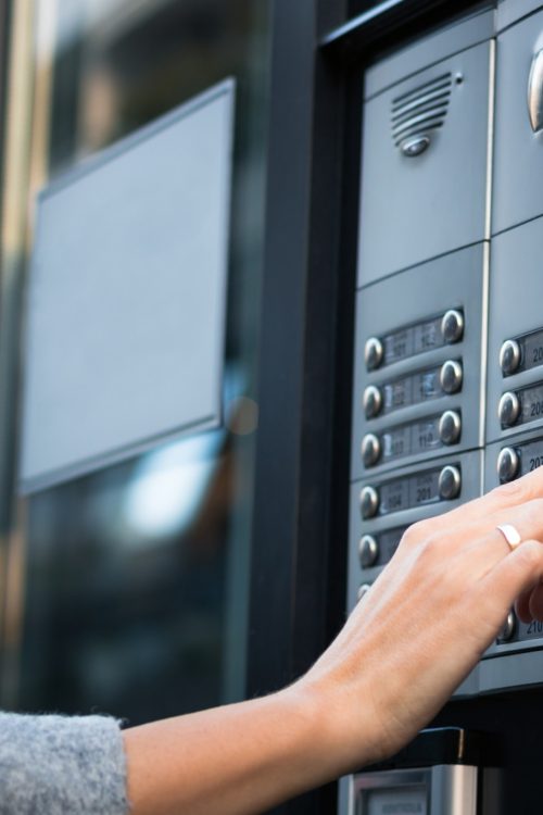 Close up of woman using intercom at residential building entrance.